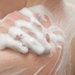 Person exfoliating shoulders with body wash during a shower.