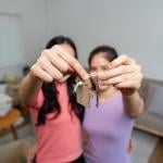 Two female friends holding keys to their new co-owned home.