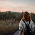A girl seen from behind with a backpack walking through nature at sunset.