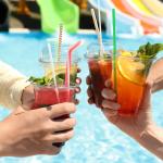 A group of friends putting up their drinks together beside a pool.