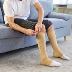 A man putting on knee-high compression stockings at home.