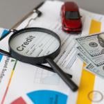 A credit loan application form with a magnifying glass, cash, and a small figure of a car on top of it.