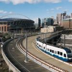 A Sound Transit Link light rail train, with the Lumen field and Seattle skyline in Washington, USA.