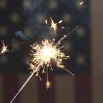 A sparkler firework with the US flag in the background for the 4th of July celebrations.