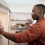 A person checking food items inside a refrigerator from the kitchen.