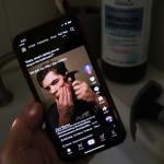 A person watching from his smartphone a video of a male TikTok influencer hammering his cheekbone, while a hydrogen peroxide bottle and a hammer are also seen in his bathroom.