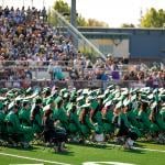  A high school graduation ceremony happening outdoors in the campus' sports field.