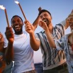 A group of friends celebrating together with sparklers during a rooftop party at sunset.