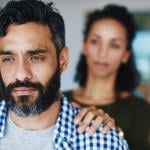 A man looking contemplative while a woman places a hand on his shoulder in a moment of emotional support.