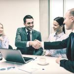 A business team with its two leaders shaking hands during a meeting.