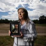 Jeanelle Couch holds framed photo of her son, David Couch, who was killed in a shooting involving a California Highway Patrol officer. She is standing in Cascade Park in Redding with a sky full of clouds and open space behind her.
