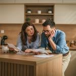 A couple reviewing bills and documents from their household finances at their home's kitchen.