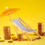 Coins around a beach deck chair and umbrella as a concept of saving for a holiday.
