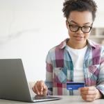 A teenager holding a credit card while shopping online from a laptop.