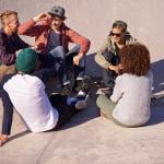 A group of adult skaters hanging out under the sun in a skate park.
