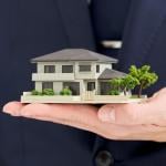 A businessman holding a small-scale figure of a house.