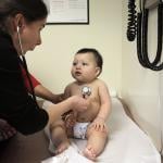 A pediatrician distracts a 9-month-old boy to check his heartbeat.