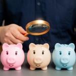 A person checking small piggy banks while using a magnifying glass, symbolizing analysis of savings.