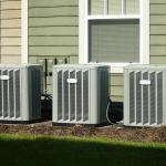 Three air conditioner compressor units placed behind a house.