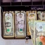 US banknotes neatly organized inside a metal cash box.