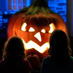 Two young girls standing in front of a giant lit up jack-o'-lantern at night.