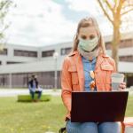 A woman wearing a mask while on a computer.