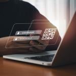 A person holding a smartphone in front of a laptop with an overlaid image of a log in screen and QR code. 