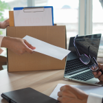 Person puts box of personal belongings on desk and hands boss resignation letter.