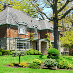 A large two-story brick and stone house with a well-manicured front lawn in an affluent neighborhood.