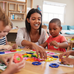 A teacher working with young students at a table in a classroom.