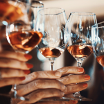 Six hands holding wine glasses for a toast.