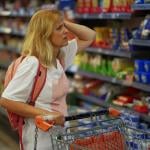 A worried looking woman touching her head while standing in front of the aisle of food in a supermarket. 