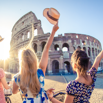 Three women wave hats at the Colosseum in morning sun.