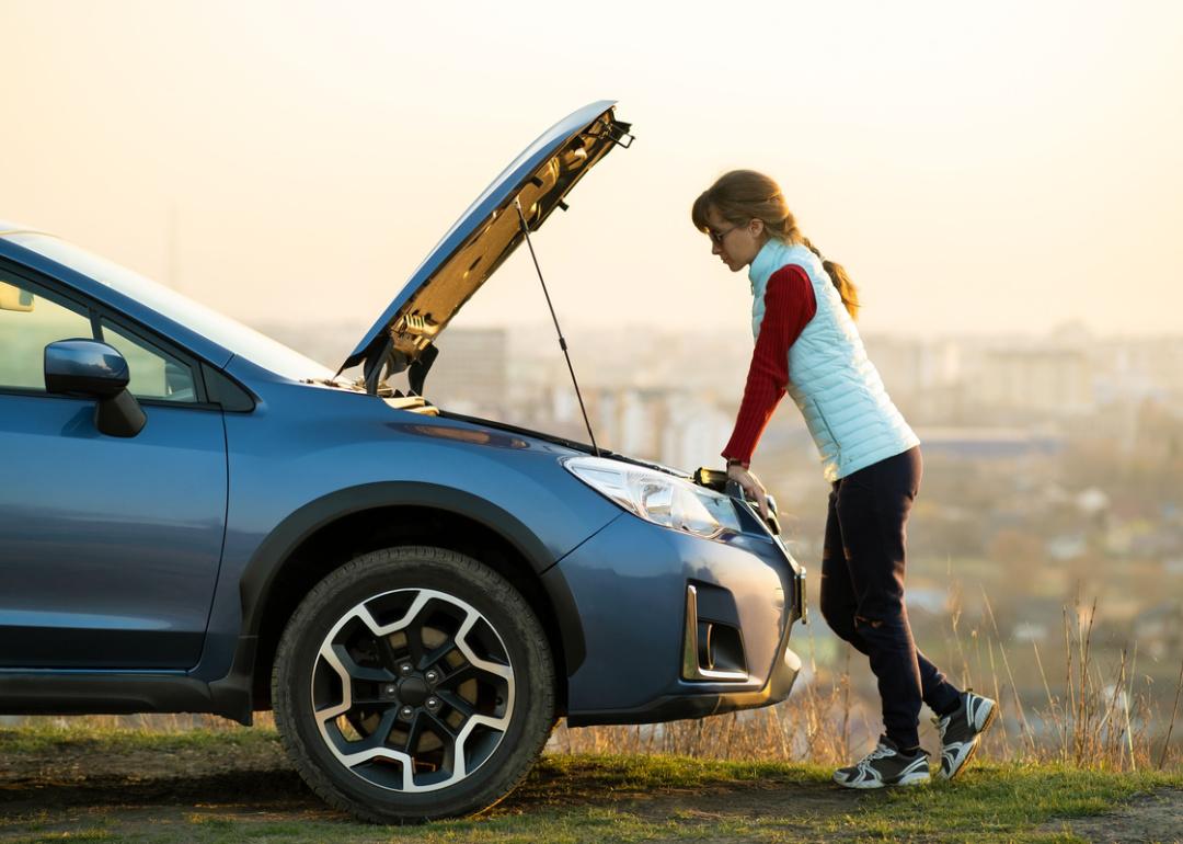 Woman standing near broken down car with popped up hood.