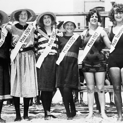 Six women pose wearing different swimsuits, with each wearing a sash that says "Miss" and the year the swimsuit was popular, including 1897, 1904, 1910, 1920, 1927, and tomorrow.