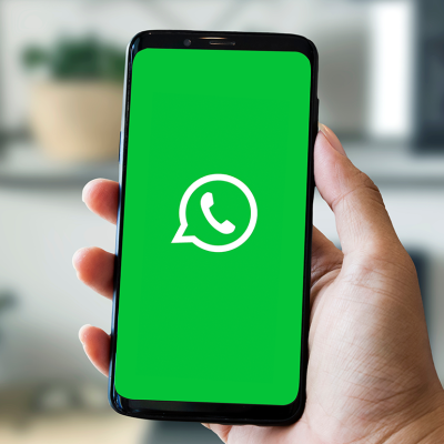 Hand holding a smartphone with a WhatsApp icon on a bright green screen.