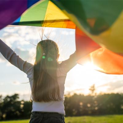 Child holding the rainbow flag against the blue sky