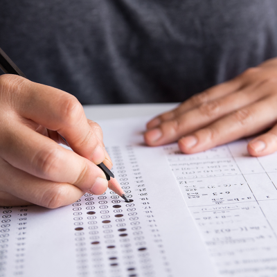 Hand with pencil filling out standardized test form.