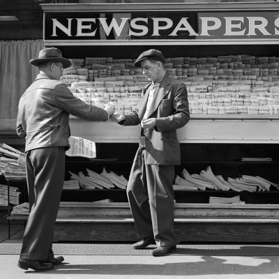 Man buying newspaper from vendor on sidewalk.