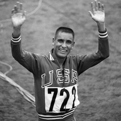 Billy Mills waving and smiling after winning the 10,000 meter race.