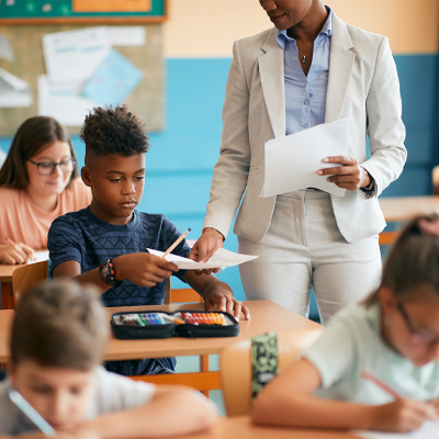 Teacher handing paper to Black student in classroom.