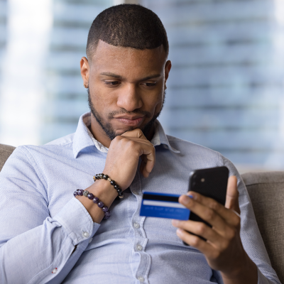 Man holding credit card and phone looking doubtful.