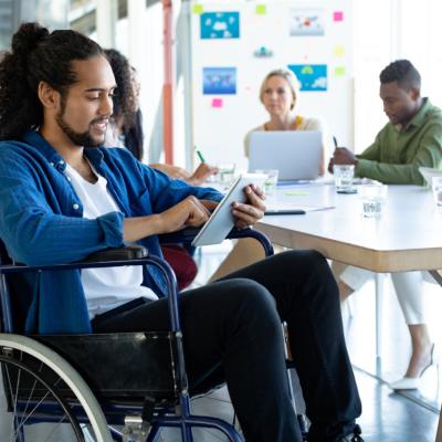 Man in wheelchair using tablet in meeting.