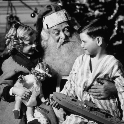 A small boy and girl sit with Santa Claus in front of a Christmas tree.