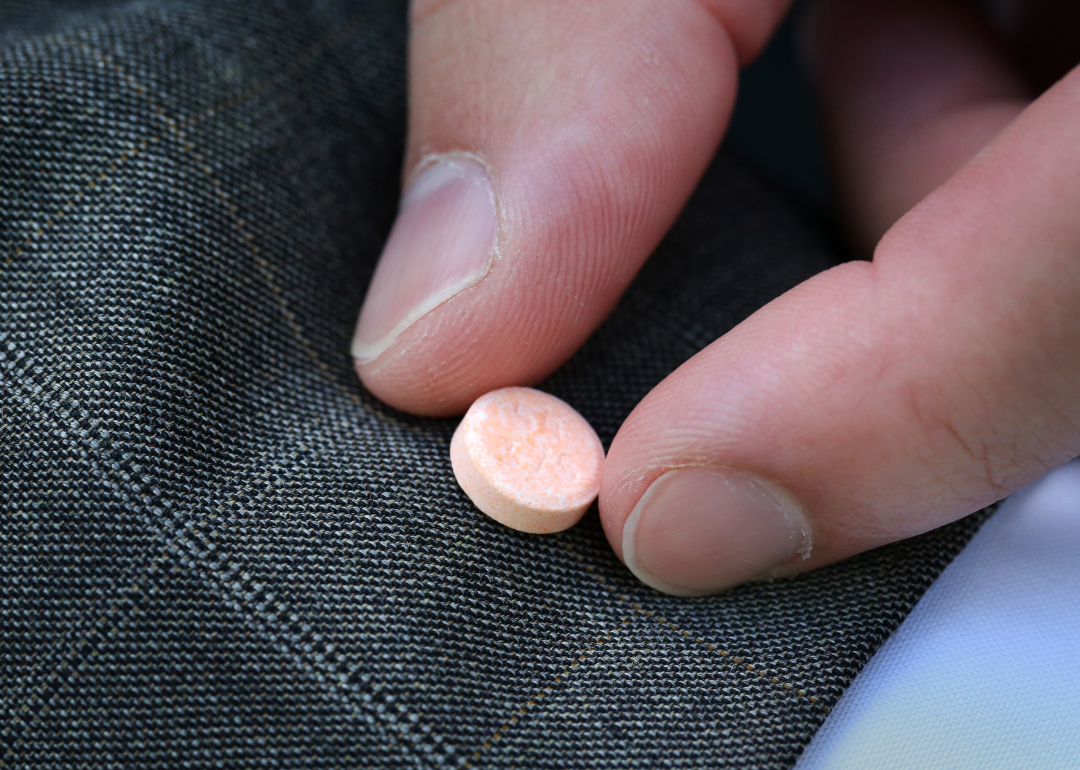 Close up of fingers picking up a small pink Suboxone pill.