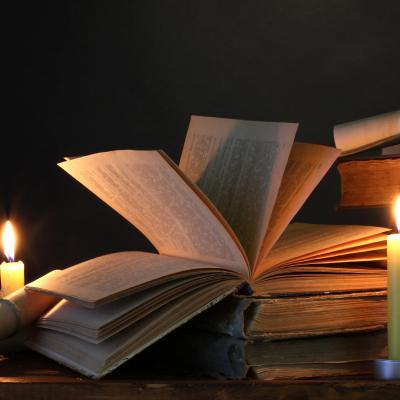 Two candles illuminate a stack of old books, with one on top open.