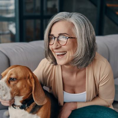 senior woman in casual clothing spending time with her dog while sitting on the sofa at home