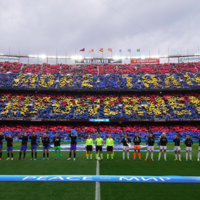 Players of FC Barcelona and Real Madrid line up as fans perform a tifo in the stands 