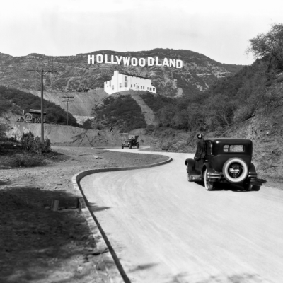 A car driving through the Hollywood Hills beneath the Hollywoodland sign.