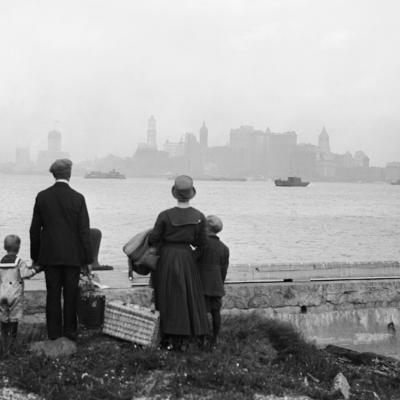 An immigrant family on the dock at Ellis Island, just having passed the examination for entry into the "land of promise." They look hopefully at New York's skyline while awaiting the government ferry.